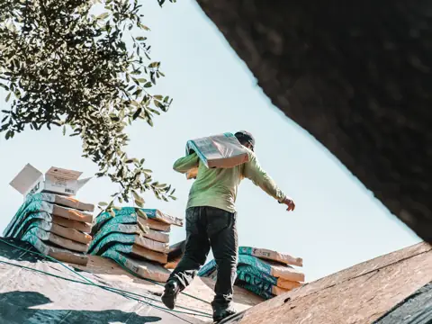 Roofer carrying a bundle of shingles across a roof